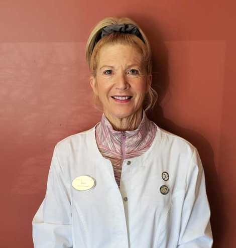 A woman in a white coat is smiling in front of a red wall.